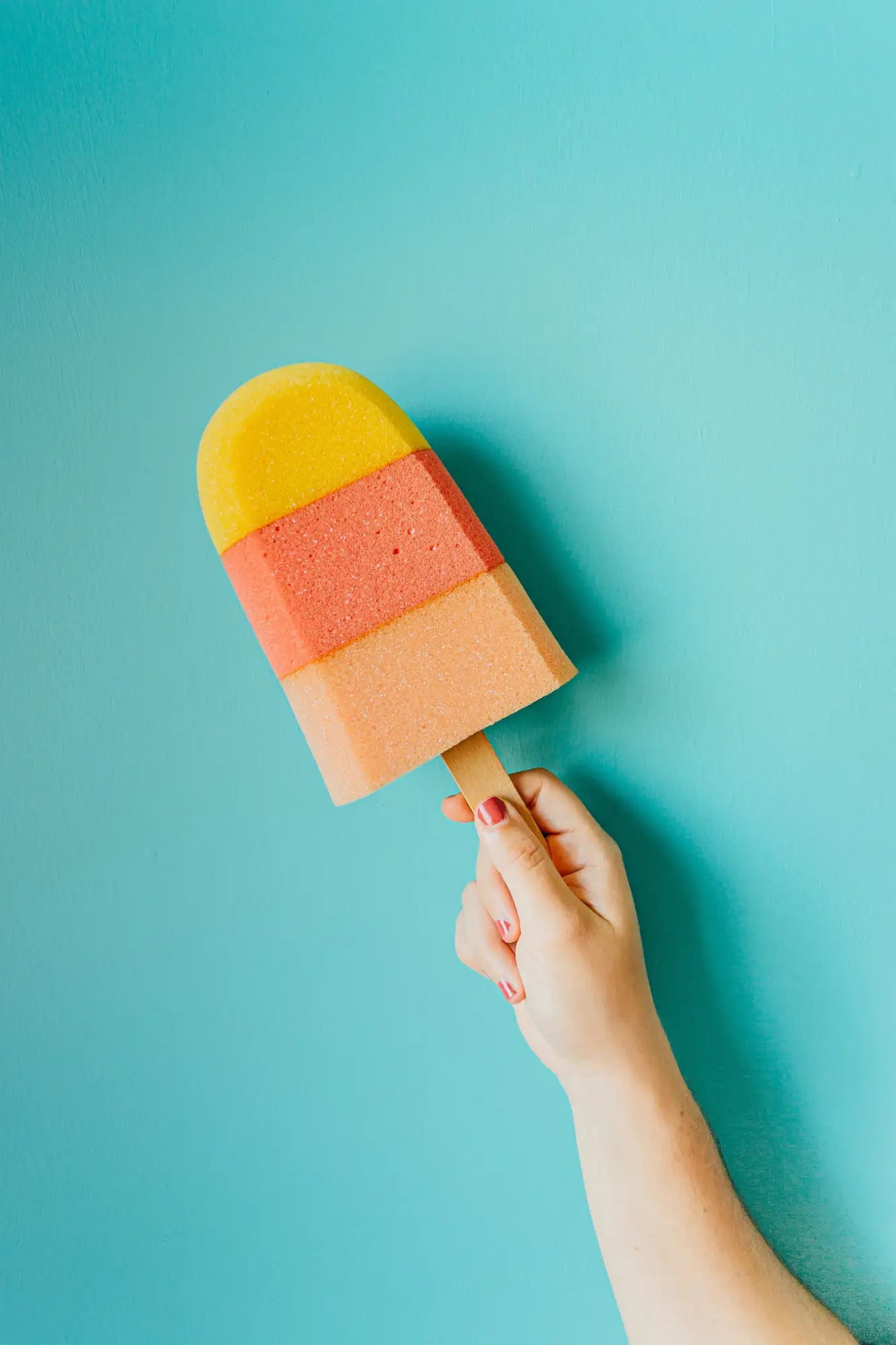 Ein buntes, dreischichtiges Schwamm-Eis am Stiel mit einem Holzstab.